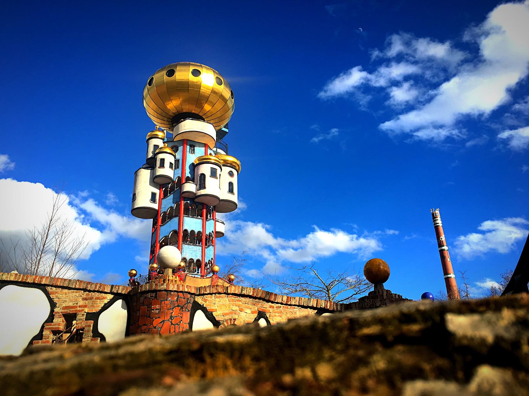 Der Kuchlbauer-Turm von Friedensreich Hundertwasser in Abensberg mit goldener Kuppel vor blauem Himmel