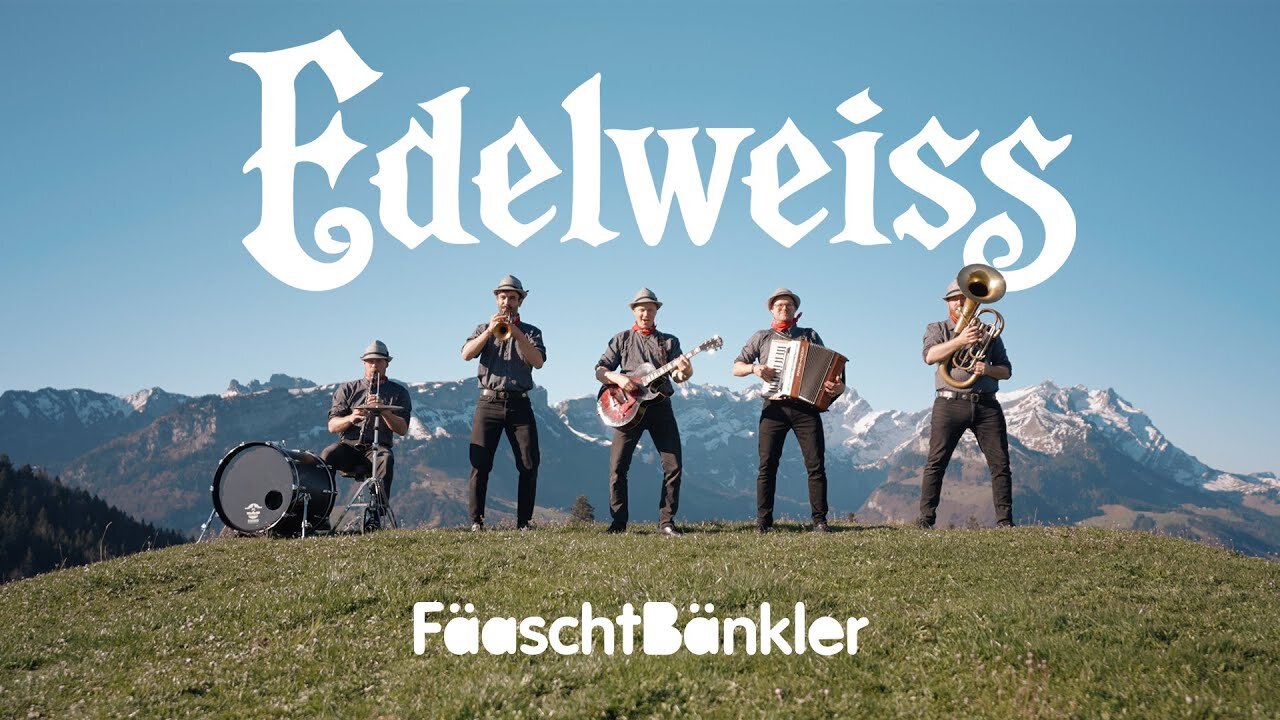 Standbild aus dem Musikvideo „Edelweiss“: die Fäaschtbänkler musizieren auf einer Bergwiese vor schneebedeckten Gipfeln