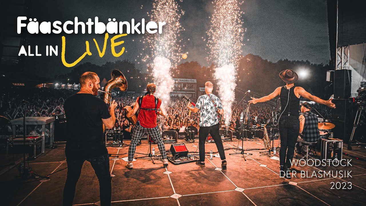 Standbild aus dem Live-Clip „All in“: die Fäaschtbänkler von hinten auf der Bühne des Woodstock der Blasmusik, vor dem Publikum steigen Funkenfontänen auf