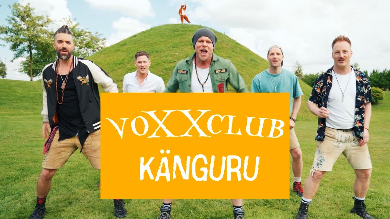 Standbild aus dem Musikvideo „Känguru“: die fünf Sänger von voXXclub in Lederhosen auf einer Wiese vor einem grünen Hügel